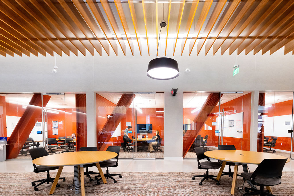 Campus learning space with tables and glass-walled study rooms.